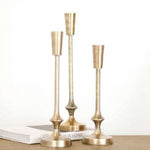 Three elegant Gold Finish Candle Pillar, Medium holders displayed on a surface with books, perfect for adding stylish decor and ambiance to any room. 1