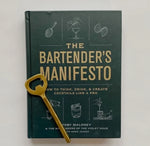 The Bartender's Manifesto book with a dark cover featuring cocktail illustrations, paired with a gold bottle opener, ideal for kitchen decor and entertaining gifts from Knotty and Board. 1
