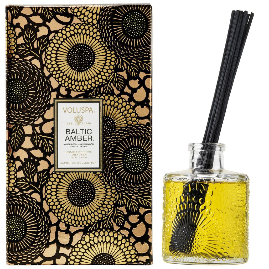 Voluspa Baltic Amber Reed Diffuser, 3.4 fl oz with amber-colored fragrance oil in a textured glass bottle and decorative black floral packaging, perfect for decor and gifts from Knotty and Board.