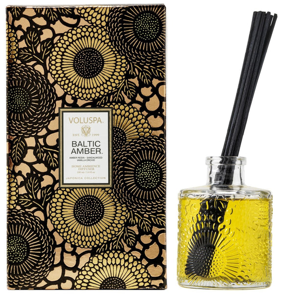 Voluspa Baltic Amber Reed Diffuser, 3.4 fl oz with amber-colored fragrance oil in a textured glass bottle and decorative black floral packaging, perfect for decor and gifts from Knotty and Board.